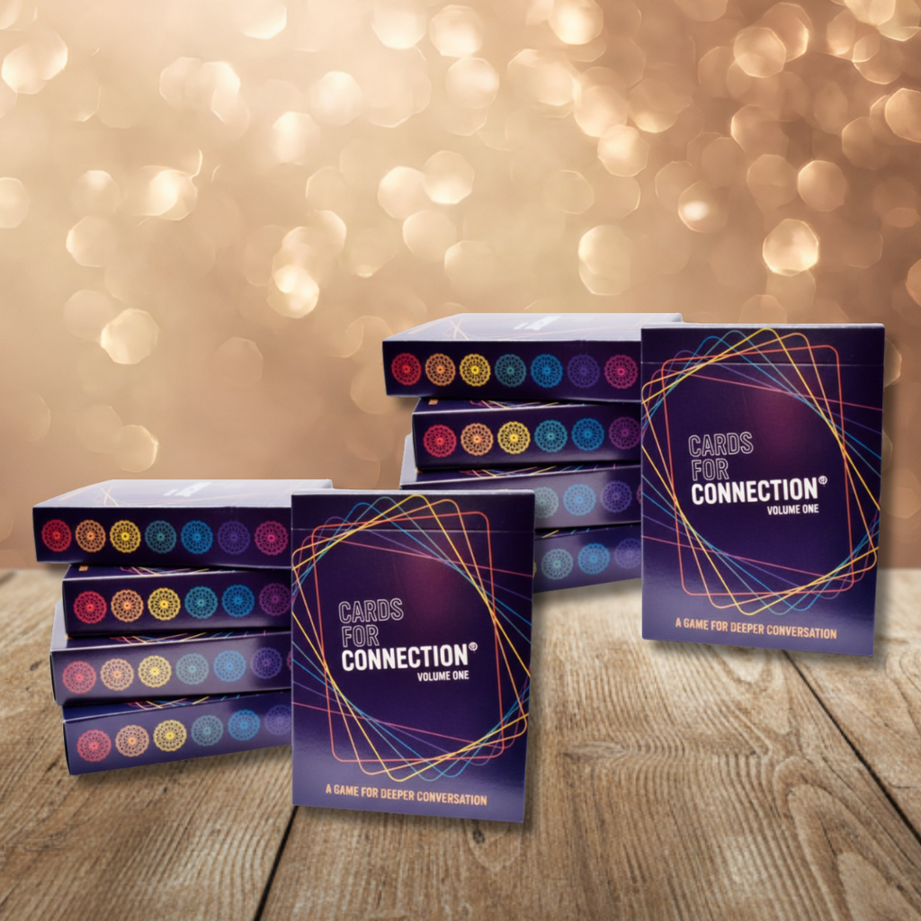 Stack of ten 'Cards for Connection' decks on a wooden surface with a blurred bokeh background.