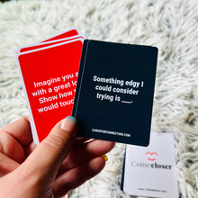 Load image into Gallery viewer, Come Closer Intimacy Deck for Couples. Hand holding two cards, one red and one black, with text, on a soft and sensual surface. Games for Humanity