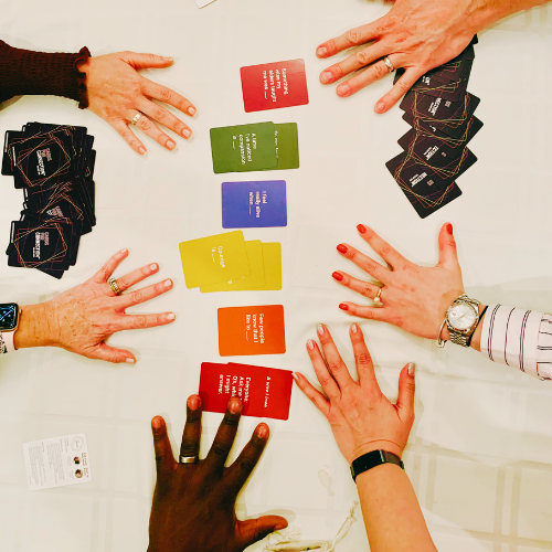 Hands of different players gathered around Cards for Connection on a cream tablecloth.