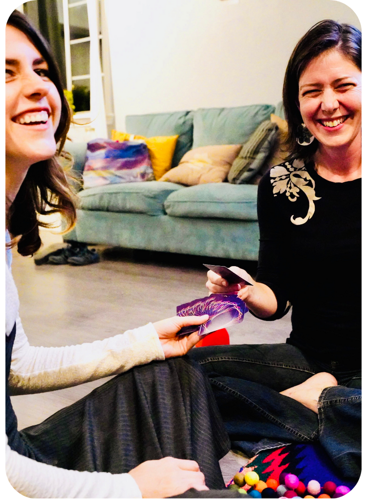 Two women are sitting on the floor playing Cards for Connection in a cozy living room setting.