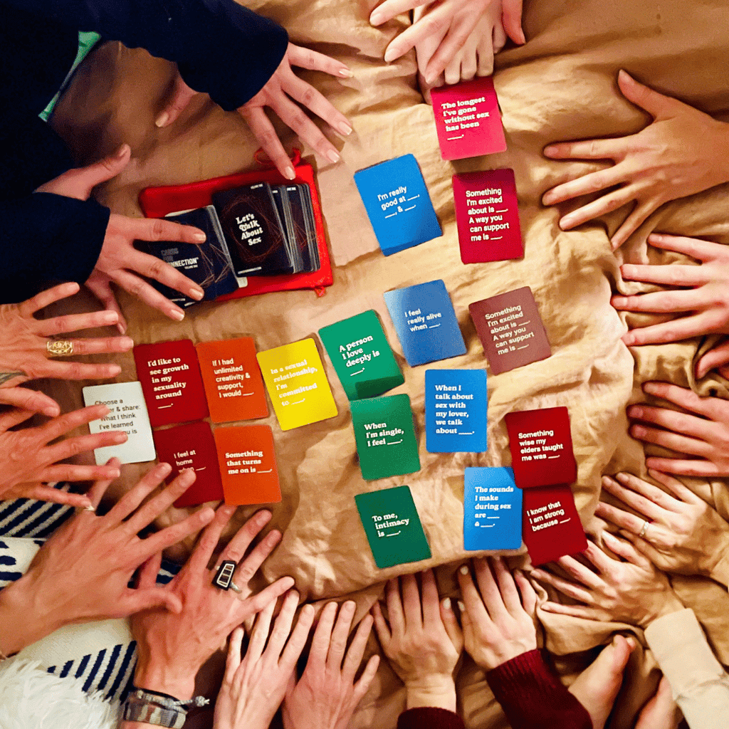 a group of friends playing with hands reaching around a rainbow spread of cards on a cloth background