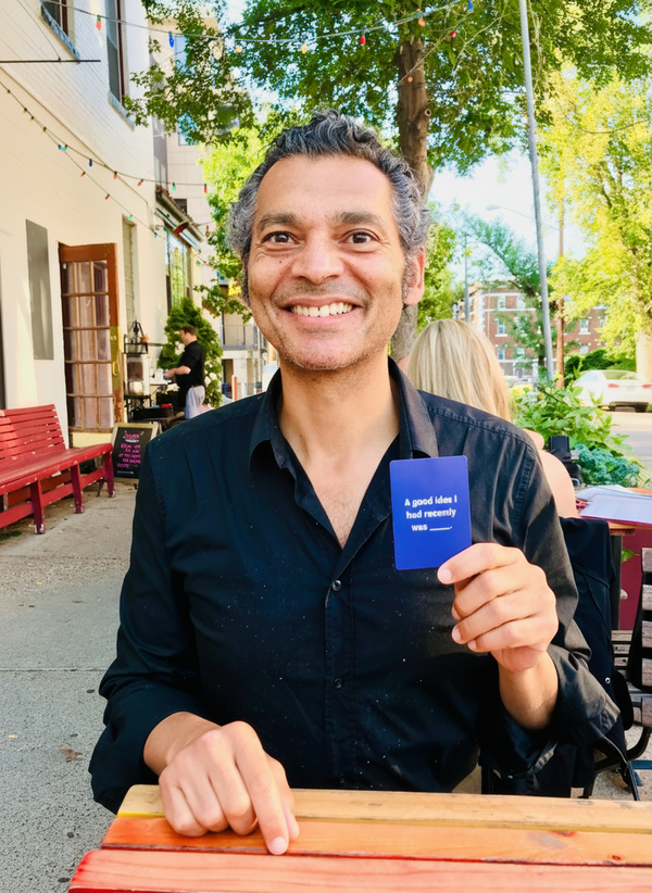 Person holding blue Cards-for-Connection card at outdoor cafe.