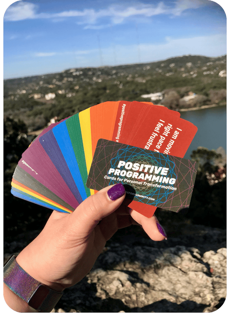 Hand holding a deck of 'Positive Programming' cards with a scenic background