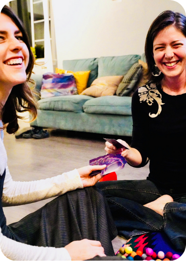 Two women sitting on a couch, one holding cards for connection, in a casual indoor setting.